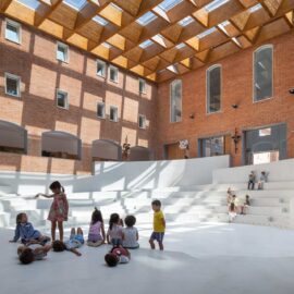 Anfiteatro interior blanco en un patio de ladrillo con cubierta superior que proyecta sombras geométricas.