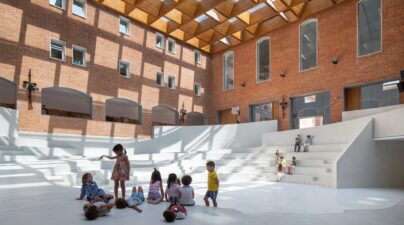 Anfiteatro interior blanco en un patio de ladrillo con cubierta superior que proyecta sombras geométricas.