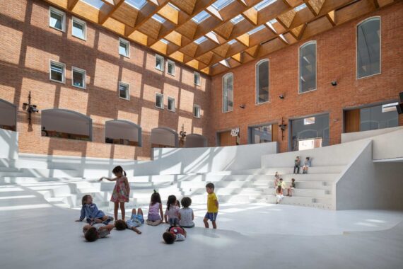 Anfiteatro interior blanco en un patio de ladrillo con cubierta superior que proyecta sombras geométricas.