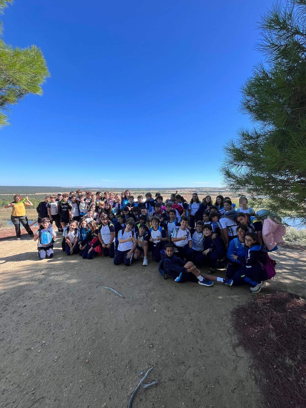 Alumnos de 6.º de Primaria posan juntos bajo los pinos, con el paisaje de Castronuño al fondo.