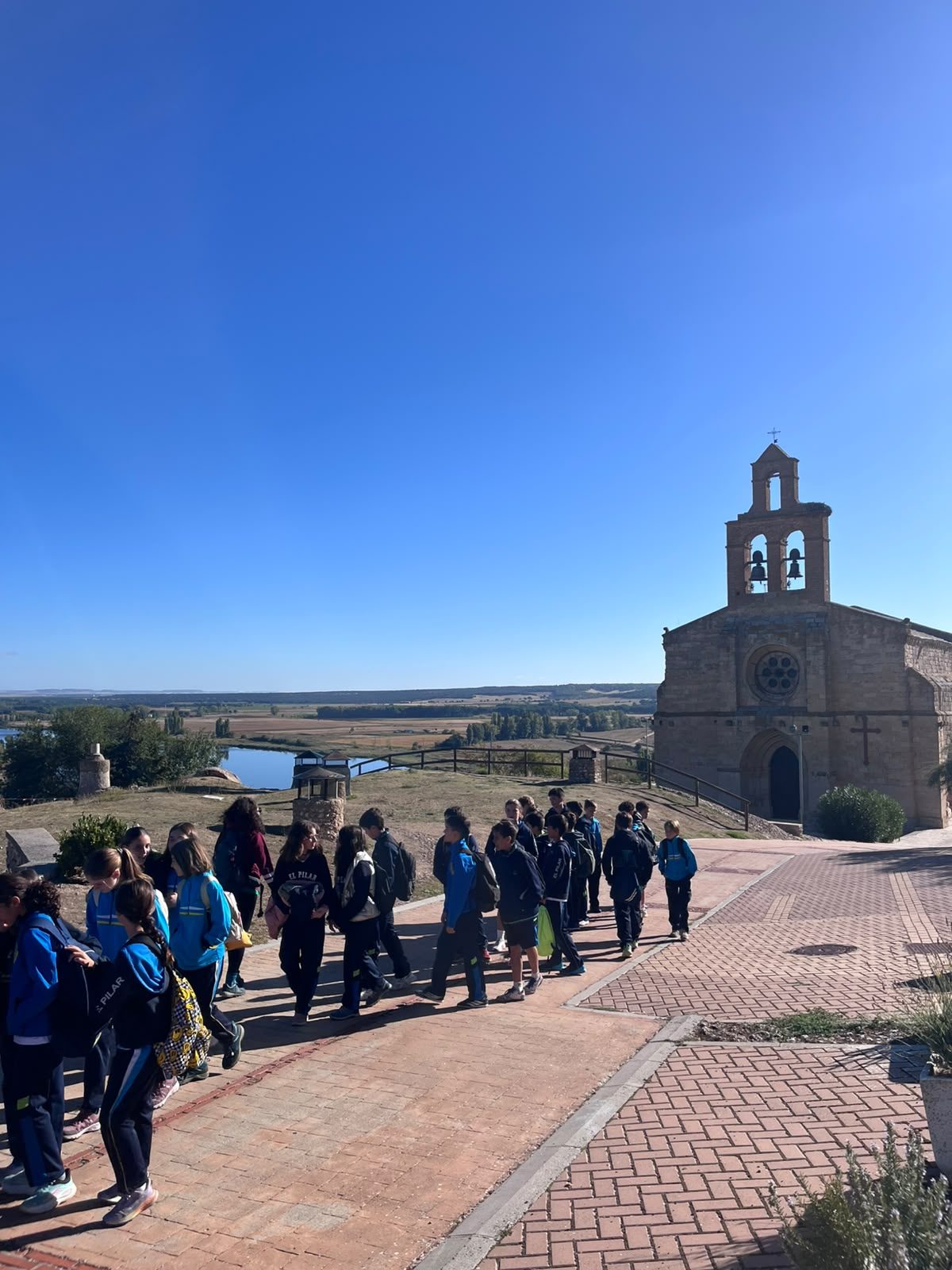 Alumnos de 6.º de Primaria caminan por una zona pavimentada junto a una iglesia de piedra en Castronuño.