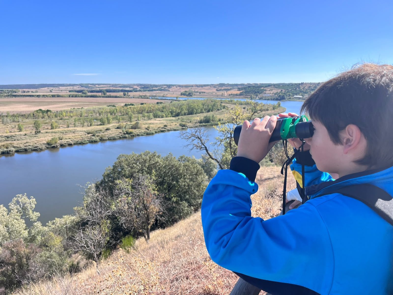 Un alumno observa con prismáticos el río Duero y la vegetación de sus orillas desde un mirador.