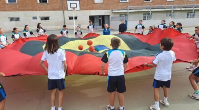 Alumnos sujetan en círculo un paracaídas de colores y hacen saltar varias pelotas sobre la tela en el patio.