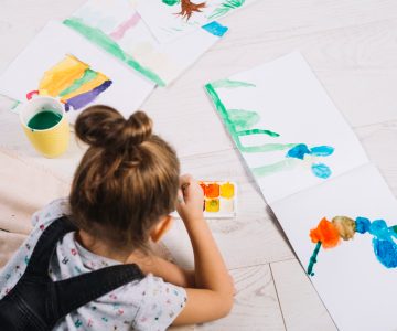 child-painting-by-water-colors-on-paper-and-lying-on-floor
