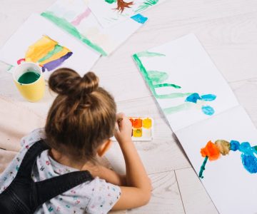 child-painting-by-water-colors-on-paper-and-lying-on-floor
