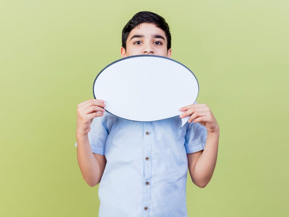 young-caucasian-boy-holding-speech-bubble-looking-at-camera-from-behind-it-isolated-on-olive-green-background-with-copy-space